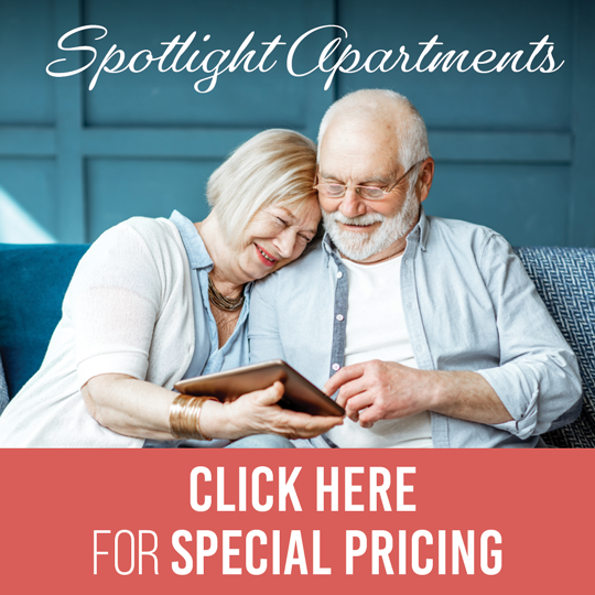 Elderly couple sitting together and smiling while looking at a tablet, with text that reads “Spotlight Apartments – Click here for special pricing.”